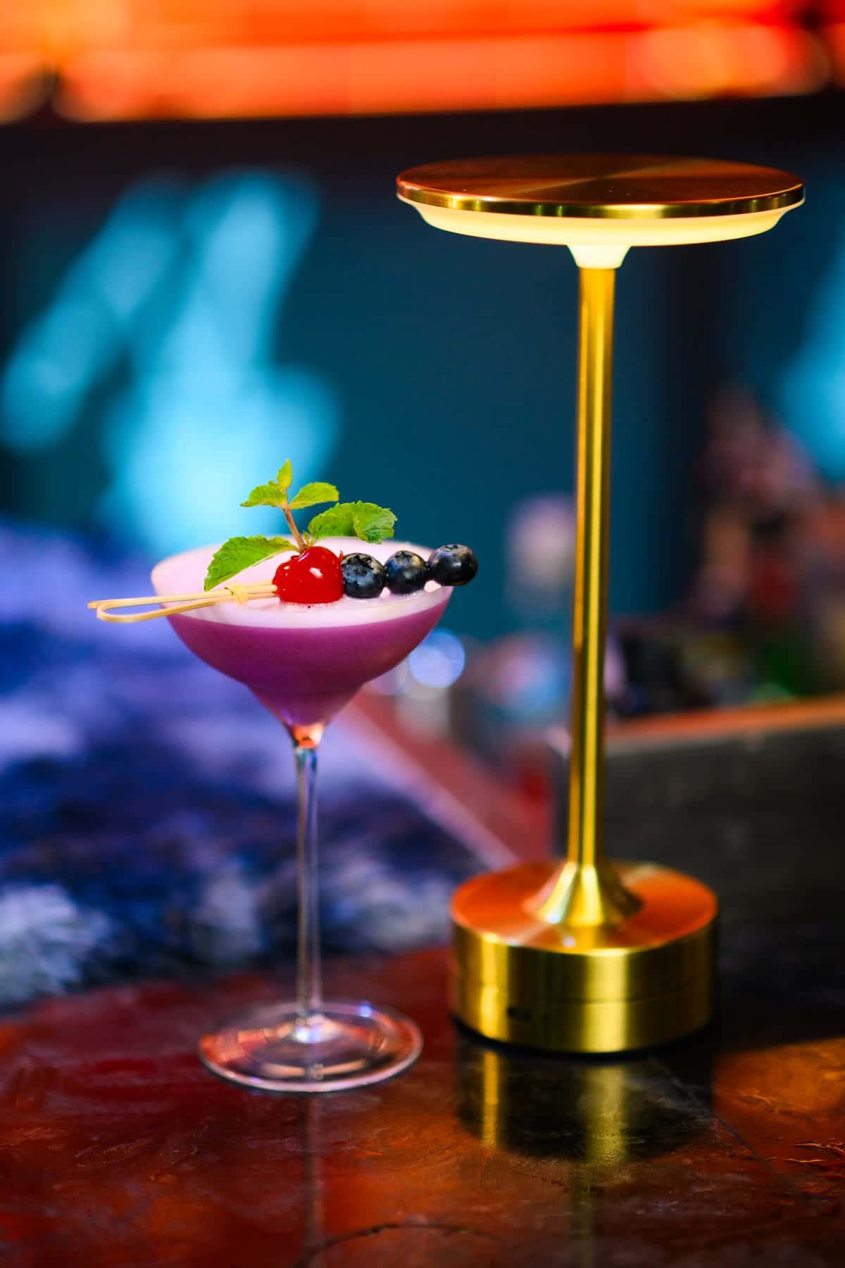 A coupe cocktail garnished with berries and mint on a lit table