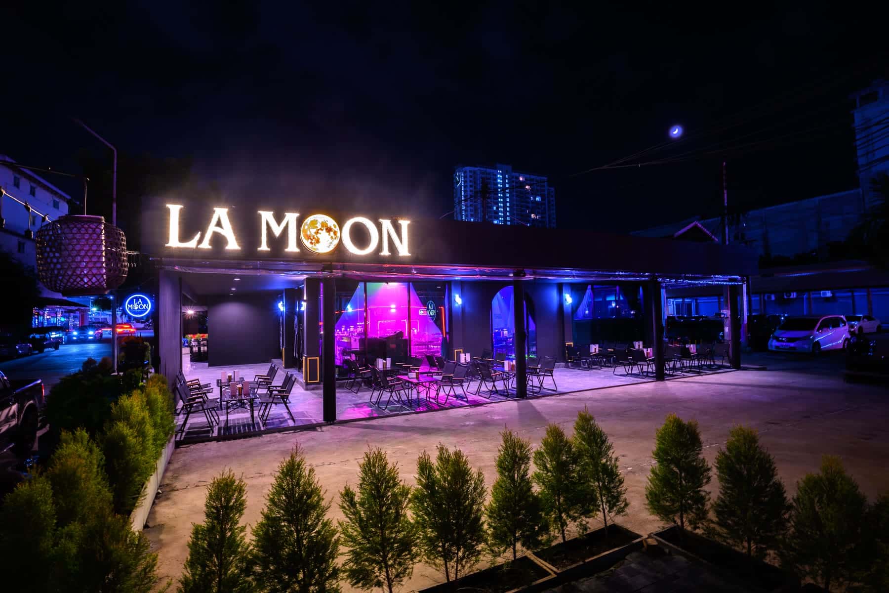 The street front of La Moon at night, its lit sign above the terrace